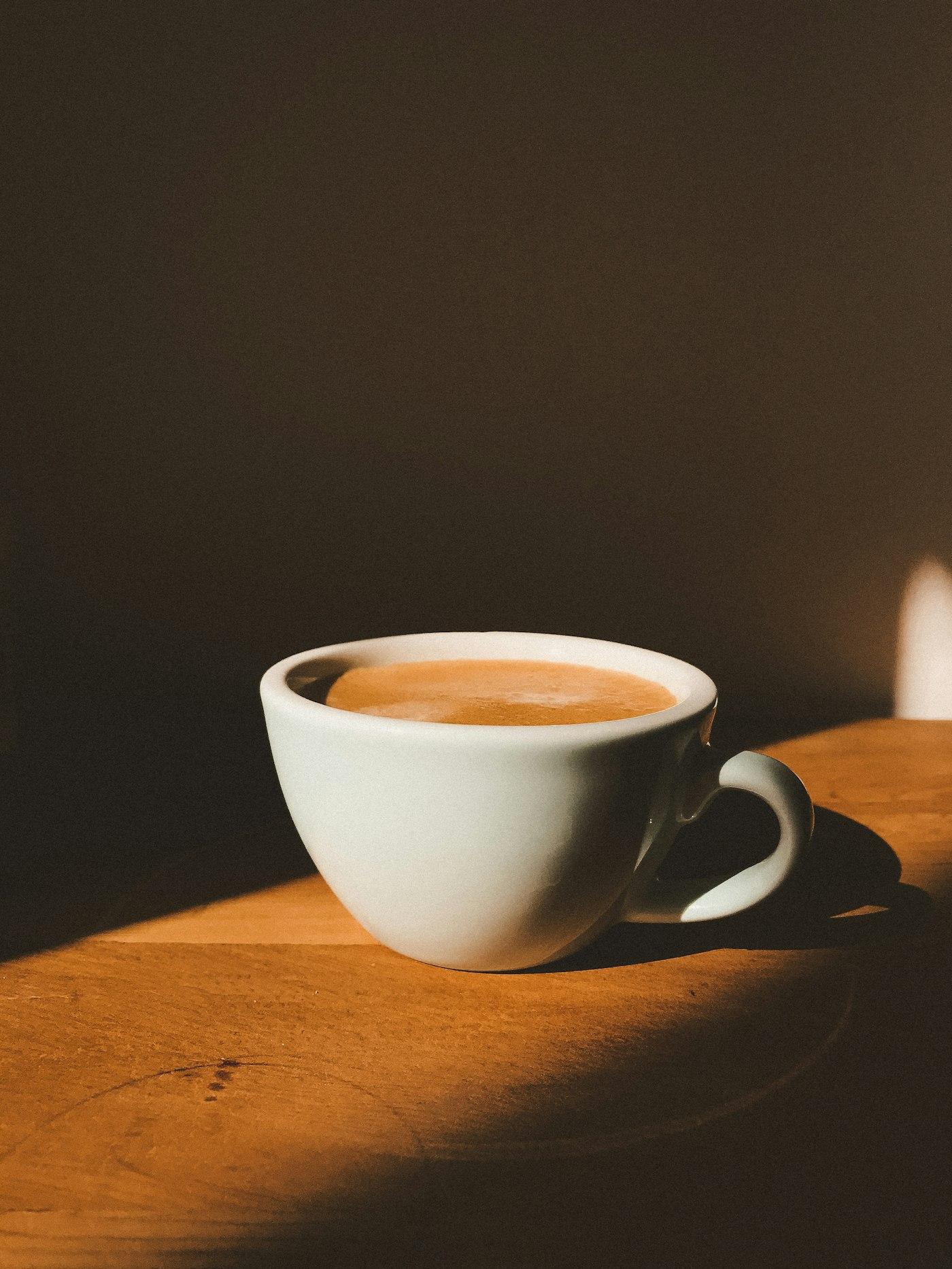Taza de café con leche sobre mesa de madera, con luz de la mañana